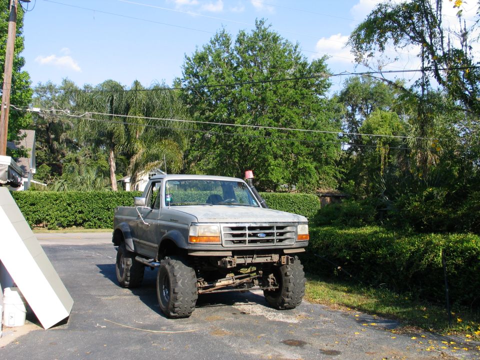 Lifted gray Ford 4x4 pickup with mud tires parked on driveway surrounded by green trees