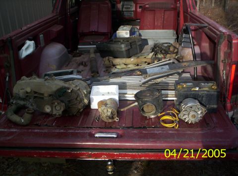 1985 Ford Bronco - Car parts are organized in the bed of a red pickup truck, ready for transport or installation.