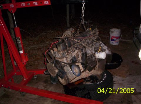 1985 Ford Bronco - Engine removed from a vehicle and suspended by a red engine hoist.