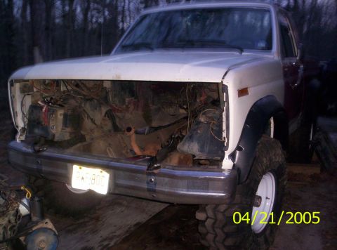 1985 Ford Bronco - This white truck, likely from the 1980s, is missing its grille and hood, revealing its engine bay.