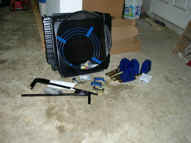 Radiator and fan assembly with blue mounting brackets and hardware on a concrete floor