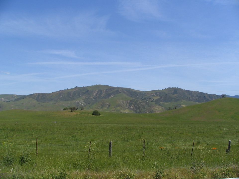 Grassy hills under a blue sky with a fence in the foreground