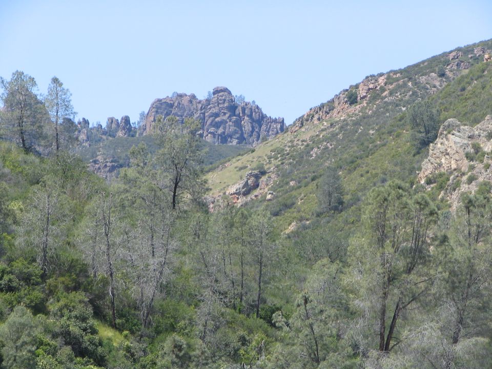 Rocky hills with scattered trees under a clear blue sky. Supermotors logo in lower right