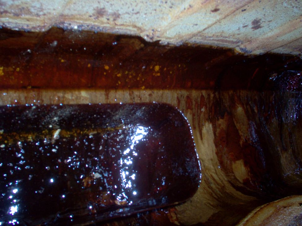 Dark sludge and brown varnish buildup along baffles inside a contaminated fuel tank