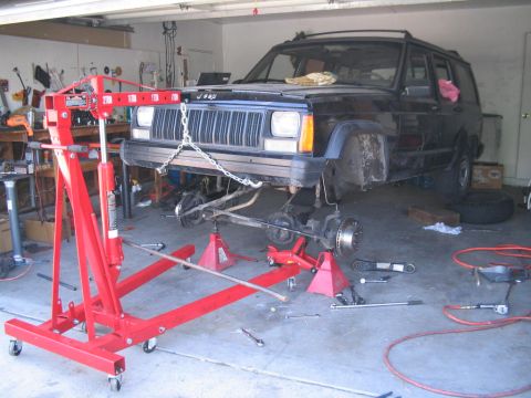 1994 Jeep Cherokee - A black Jeep Cherokee is undergoing front-end repairs in a garage, with its axle removed and supported by stands.