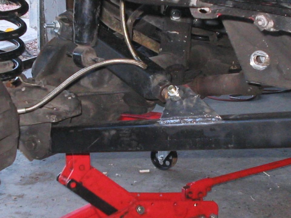 Vehicle frame and suspension parts on a red jack, showing welded brackets and brake lines