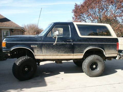 1991 Ford Bronco - Side profile of a lifted 1991 Ford Bronco with large off-road tires.