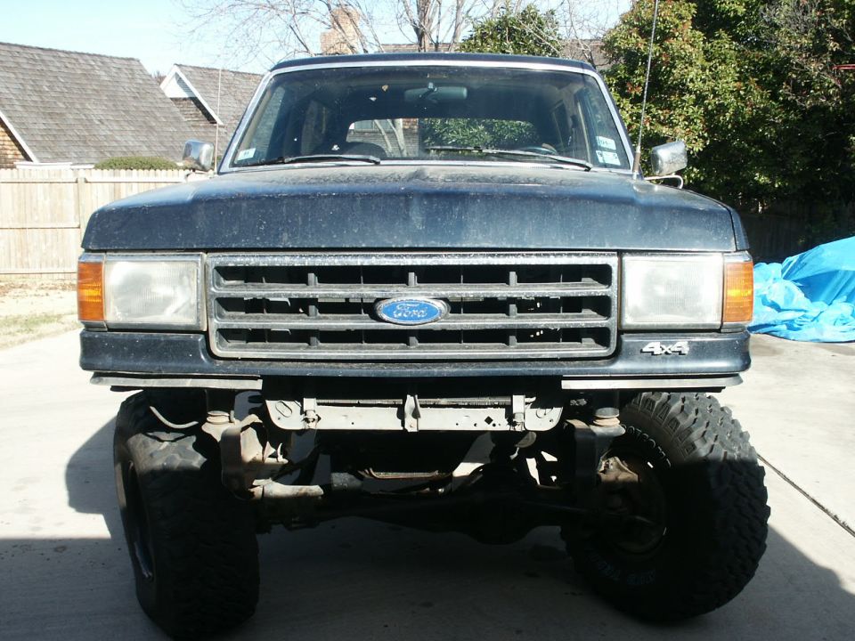 Lifted dark blue Ford Bronco with front bumper removed showing exposed frame horns and front axle