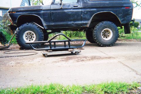 1978 Ford Bronco - A black 1978 Ford Bronco sits with a new bumper nearby, ready for installation.