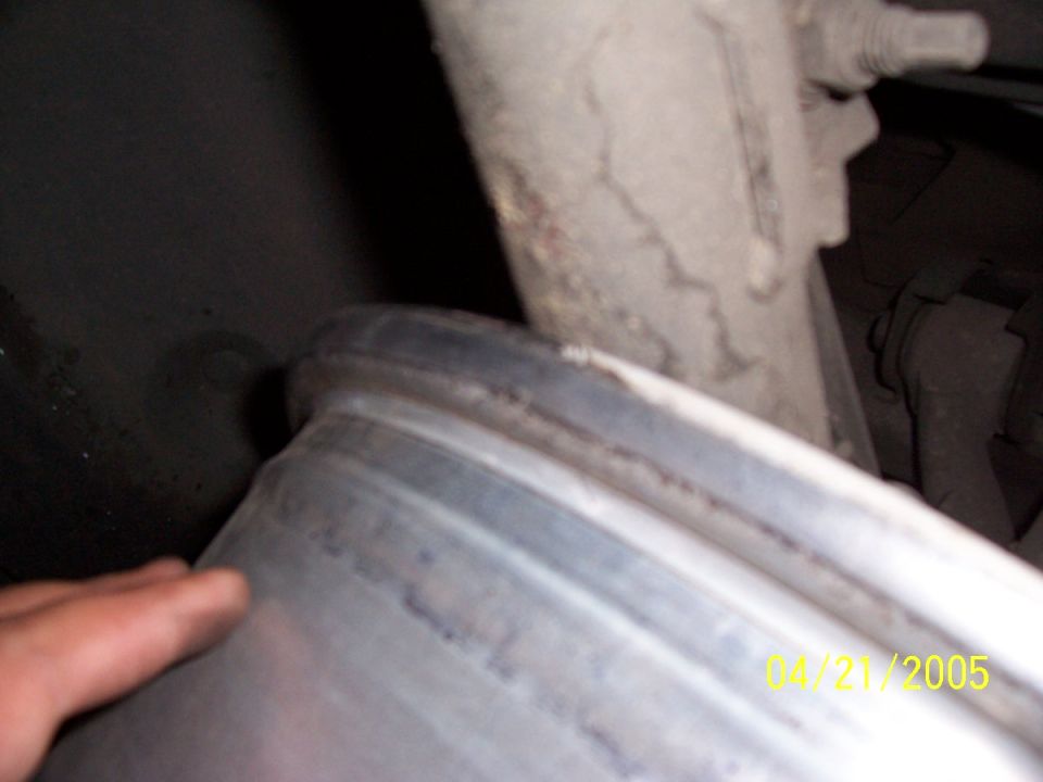 Close-up of aluminum cylindrical vehicle part with a hand at lower left, cast bracket behind.