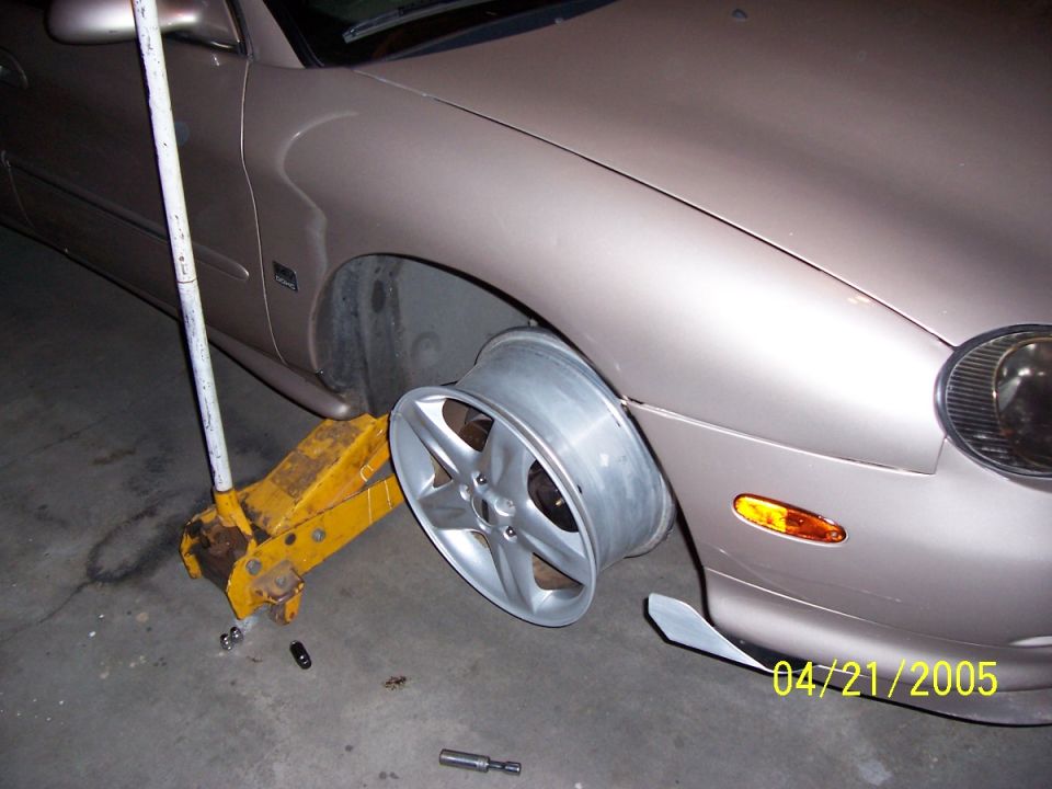 Car on jack with front wheel removed, showing flat tire