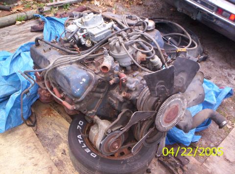 1985 Ford Bronco - A V8 engine assembly, likely removed from a vehicle, is shown outdoors on a tire and tarp.