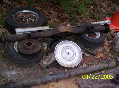 1985 Ford Bronco - Various vehicle parts, including a rear axle assembly, tires, and an air cleaner, are laid out on the ground.