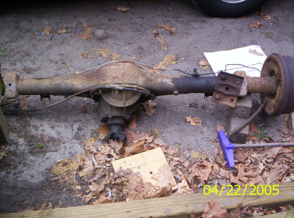 Rusty rear axle assembly with drum brake, resting on wood blocks and leaves