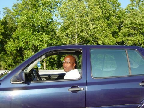 1988 Ford Bronco - A man drives a blue SUV on a sunny day with trees in the background.