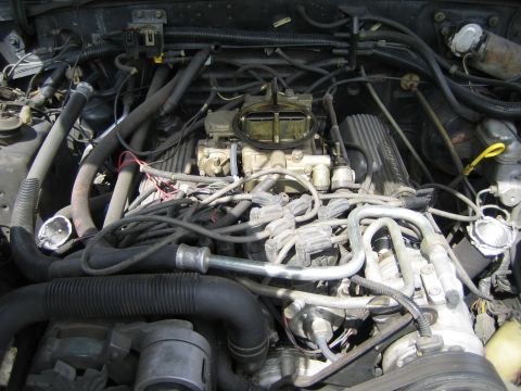 1985 Ford Mustang - Close-up view of a cluttered engine bay, showing various hoses, wires, and engine components.
