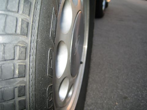 1985 Ford Mustang - A side view of a car wheel and tire, with another vehicle partially visible in the distance.