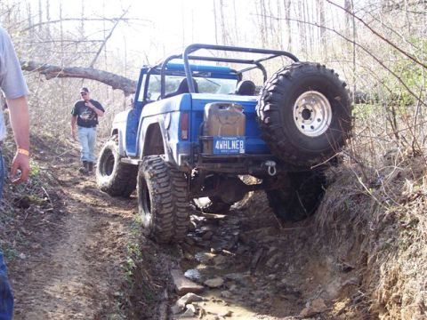 1974 Ford Bronco - An off-road vehicle tackles a challenging dirt path with trees and brush surrounding it.