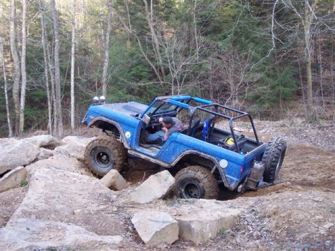 1974 Ford Bronco - A blue off-road SUV with a roll cage is shown navigating a challenging rocky trail.