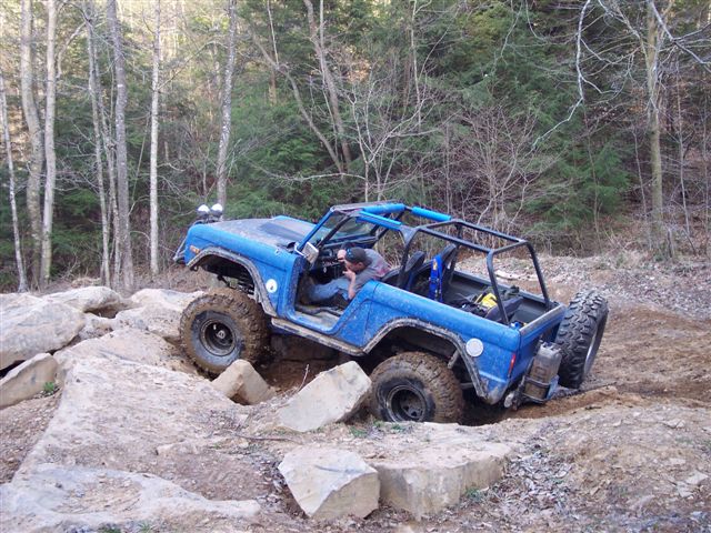 Blue off-road SUV with roll cage navigating rocky terrain