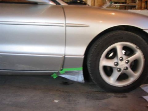 1993 Ford Probe - A close-up view of a silver car's side panel and wheel, with green tape applied to the lower body trim.