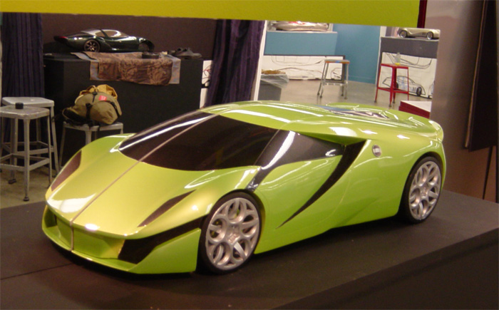 Green low-slung concept supercar model on display stand in a studio with workbenches behind