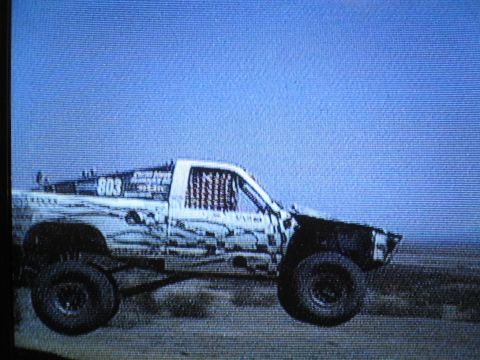 1990 Ford Bronco - grainy screen image of an off-road race truck marked 803 driving across blue-tinted desert terrain.