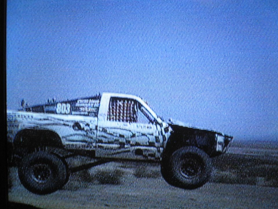 Number 803 off-road race truck driving in the desert, grainy screen photo