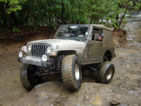 1989 Ford Bronco - A mud-covered Jeep Wrangler TJ navigates a challenging off-road trail.