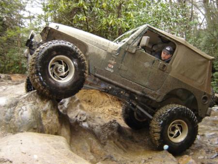 1989 Ford Bronco - A Jeep Wrangler navigates a challenging off-road course, with one wheel high in the air.
