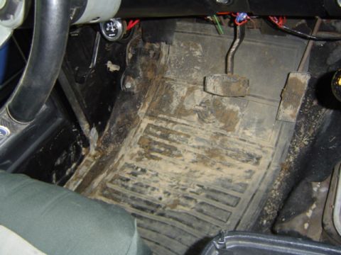 1979 Ford Bronco - The interior floor mats and pedals are covered in mud, suggesting recent off-road use.