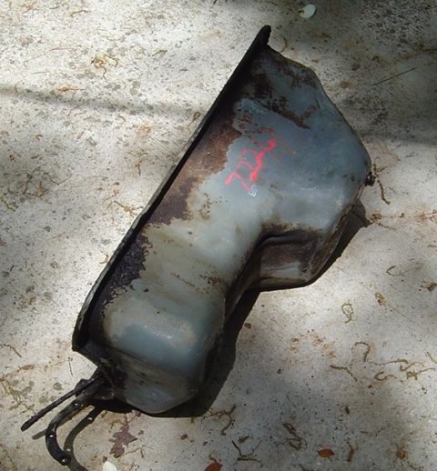 1986 Ford Bronco - This is a rusted fuel tank with red markings on it, lying on concrete.