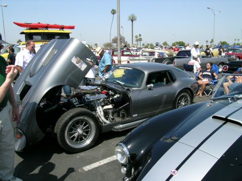 1993 Ford Probe - A gray coupe displays its engine with the hood open, parked next to a black and silver striped car at an outdoor event.