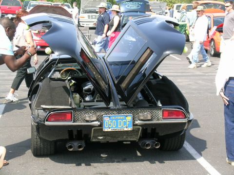 1993 Ford Probe - Black De Tomaso Pantera with butterfly doors open at an outdoor car show.