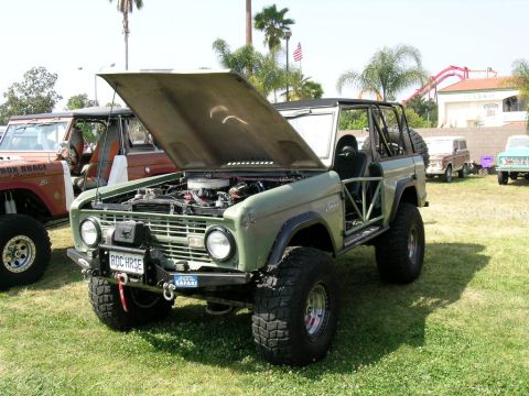 1993 Ford Probe - Modified green Ford Bronco parked on grass with other vehicles and a roller coaster in the background.