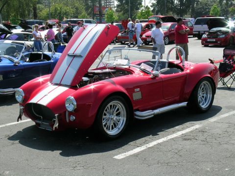 1993 Ford Probe - A red convertible with white racing stripes is displayed with its hood open at a car show, with other vehicles visible in the background.