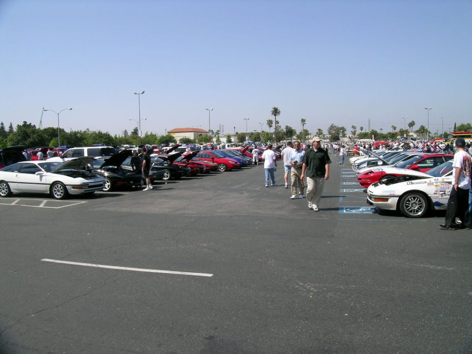 Rows of sports cars and a crowd at an outdoor car show in a sunny parking lot