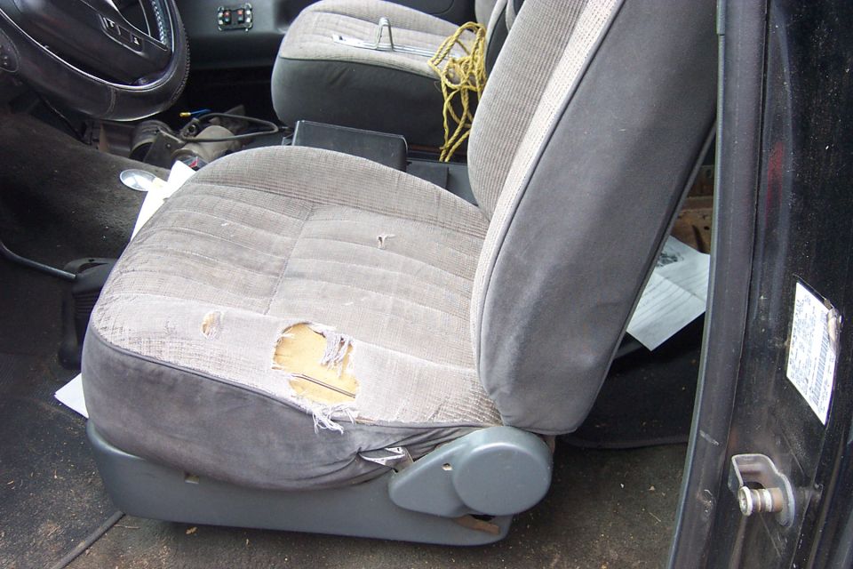 Worn gray cloth driver bucket seat with torn cushion inside a truck cab