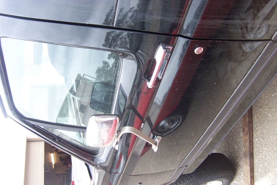 Close low-angle of a dark vehicle's A-pillar, windshield, side mirror and body in a garage