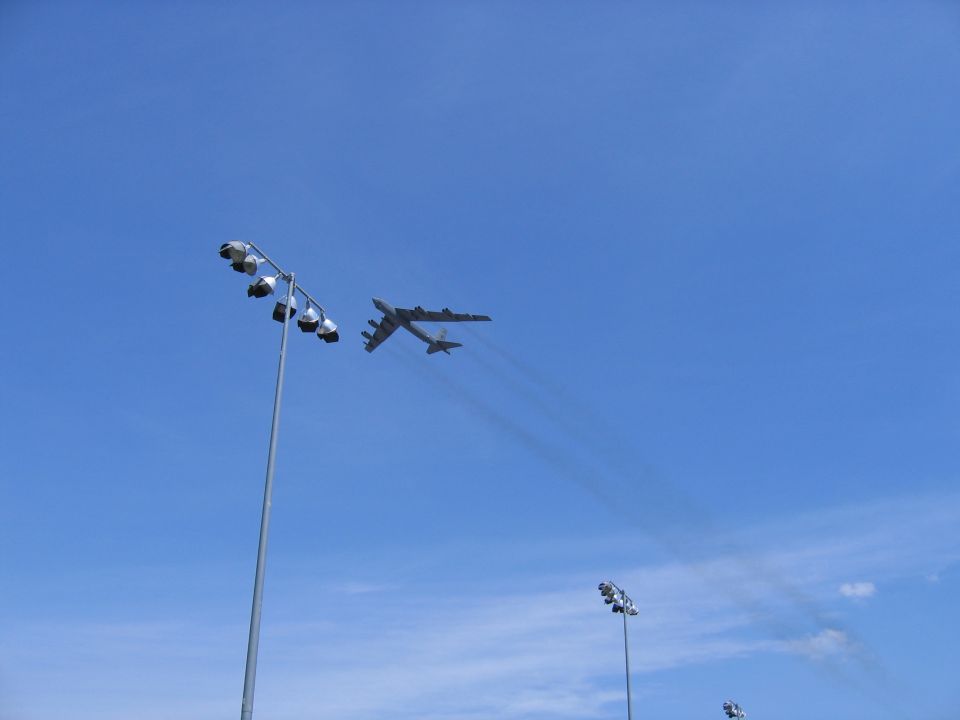 B-52 bomber flies in blue sky with stadium lights