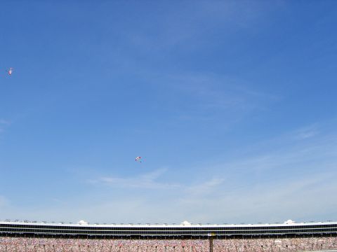 2000 Ford Crown Victoria - Two parachutists descend under a clear blue sky above a packed stadium.