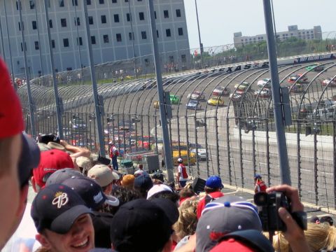 2000 Ford Crown Victoria - A race is underway at Texas Motor Speedway, with multiple cars visible on the track and spectators in the foreground.