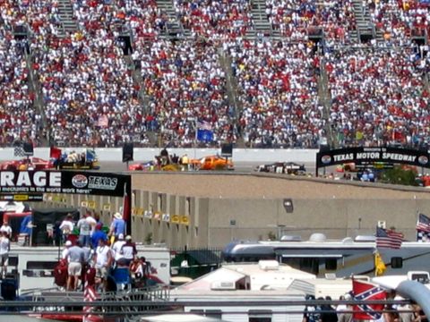 2000 Ford Crown Victoria - Race cars are visible on the track at Texas Motor Speedway, with a packed stadium of spectators in the background.