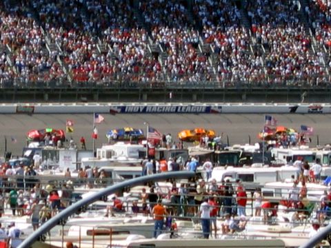 2000 Ford Crown Victoria - Spectators fill the stands at the Indy Racing League track, with RVs and support vehicles visible below.