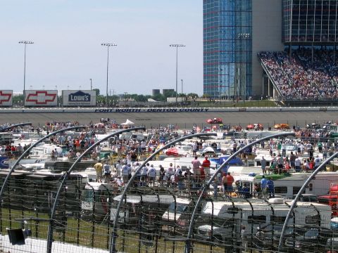 2000 Ford Crown Victoria - A crowded scene at a race track, showing RVs parked and people gathered, with a large building and stadium in the distance.
