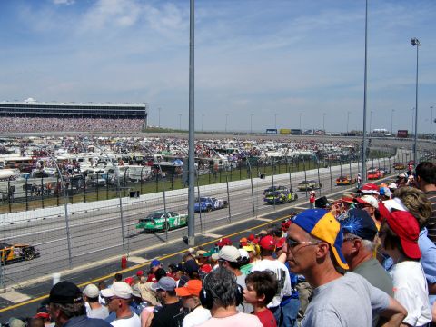 2000 Ford Crown Victoria - A race is underway at a speedway with many cars on the track and a large crowd in the stands.