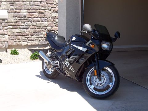 1994 Ford Bronco - A black Suzuki motorcycle is parked outside a garage, with a stone wall in the background.