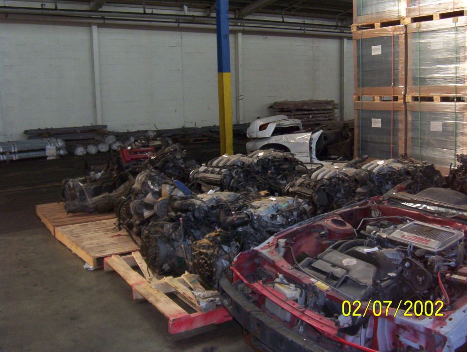 Pile of car engines in a warehouse, with a red car front in foreground