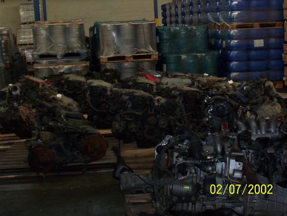 pile of car engines in a warehouse with stacked goods in background
