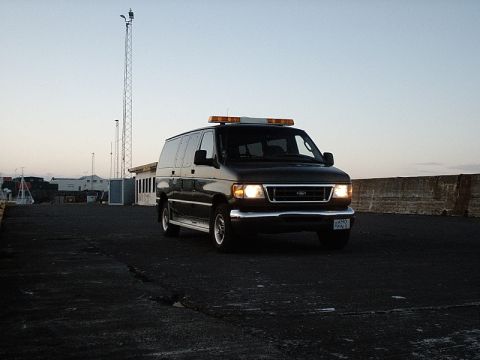 1996 Ford Bronco - A dark van with an amber light bar on its roof is parked on an asphalt surface near a concrete barrier.